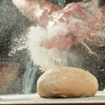 New laws surrounding flour dust limits will come into effect later this year. Pictured is a close up of a baker's hands covered in dust. They are over the top of bread dough, and are being clapped together. Flour dust has been spread everywhere.