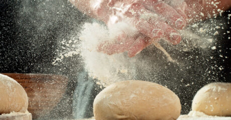 New laws surrounding flour dust limits will come into effect later this year. Pictured is a close up of a baker's hands covered in dust. They are over the top of bread dough, and are being clapped together. Flour dust has been spread everywhere.