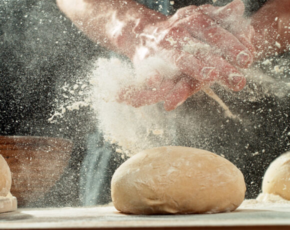 New laws surrounding flour dust limits will come into effect later this year. Pictured is a close up of a baker's hands covered in dust. They are over the top of bread dough, and are being clapped together. Flour dust has been spread everywhere.